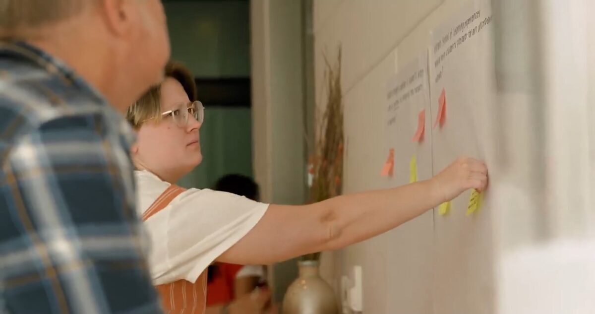 A participant adding reflections to a shared wall of sticky notes during a community-building exercise.