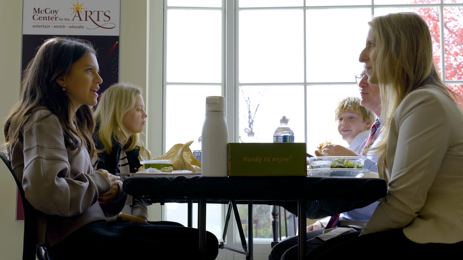 A student and educators talking over lunch beneath the McCoy Center for the Arts banner.